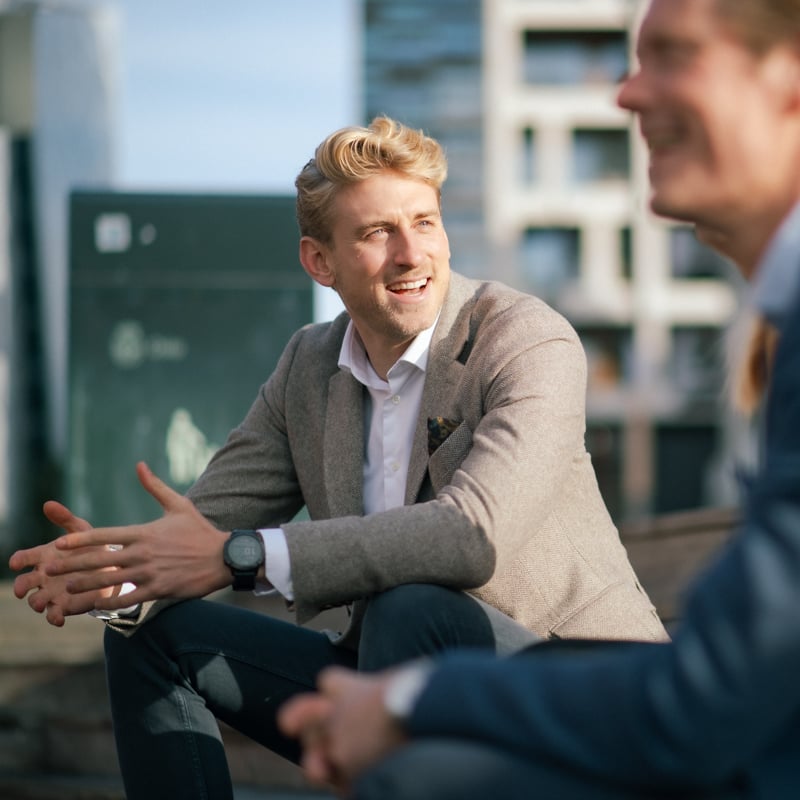 Nærbilde av en mann i beige jakke som sitter og smiler